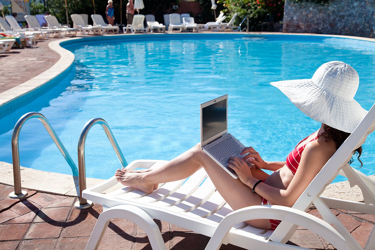 Young woman in big hat relaxing near the pool with laptop